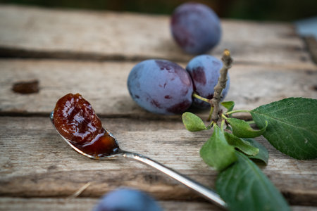 plum jam in a white ceramic pot on an aged wooden background, fresh plums near