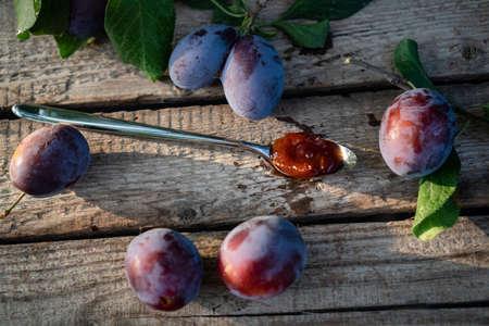 dessert steel spoon with plum jam on an aged wooden background, fresh plums nearの写真素材