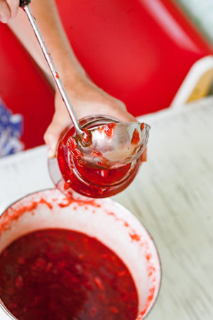 pour fresh strawberry jam into a jar with steel ladle