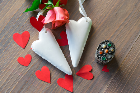 Two porcelain white hearts on the wood textural table with pink flower and many red paper hearts around. Wedding or love sign. Flat lay.の写真素材