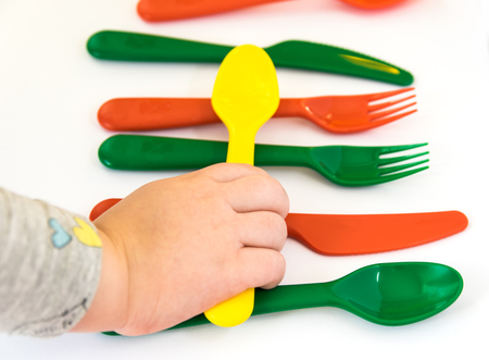 Plastic yellow spoon in hand of the small child. Colorful tableware on the white background.の写真素材