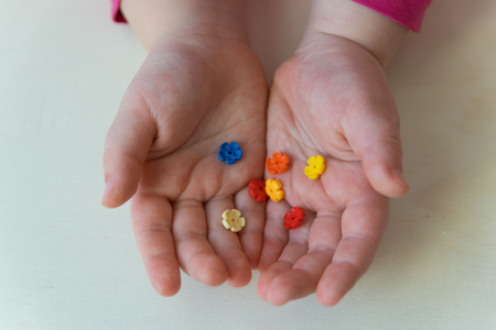 Hands on the wood background. Colorful plastic flowers in the child hands.の写真素材