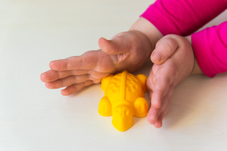 Hands of the child holding the little toys on the wood background. Yellow plastic turtle.の写真素材