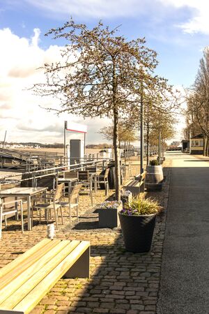 A street near the river in spring time. Sun weather. The quay with summer cafe, flower, trees, bench, tables and chairs.の写真素材