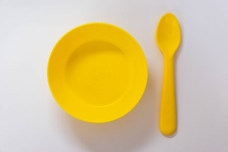 Plastic yellow spoon located near yellow plate on the white background. Flat lay. Top view.の写真素材