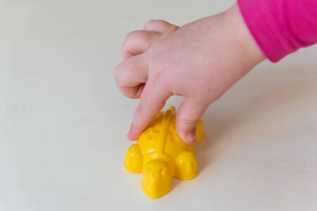 Hands of the child holding the little toy on the wood background. Yellow plastic turtle in the child hands.の写真素材