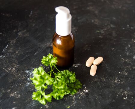 Brown glass bottle with essential oil or creme, vitaminen and healing green herbs on the dark rough texture background.の写真素材