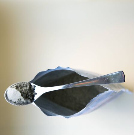 Metal spoon on the package with green herbal natural powder on the light background.の写真素材