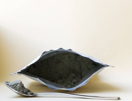 Iron little spoon with green herbal powder in the package on the light background.の写真素材
