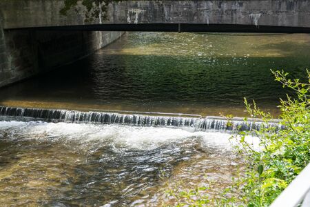 Beautiful waterfall on the summer landscape with old bridge. Nature background. Falls with clean water in sunny day and much green trees around.の写真素材