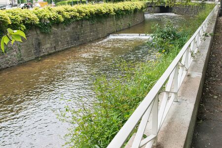 A little old waterfall in the summer city with old bridge. Nature background. Falls with clean water in sunny day and green grass around.の写真素材