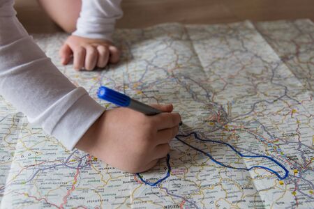 Hand of the child writing on a map with blue pen. Kids hand holding felt-tip pen. Travel and vacation  with children. Summer rest concept.の写真素材