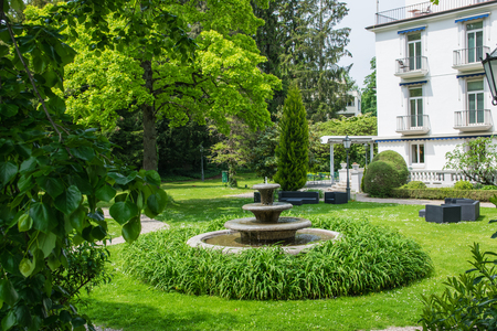 Fountain and summer garden near a hotel in Baden-Baden. Nature background with vintage lamps, trees, flowers and green grass.のeditorial素材
