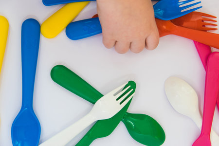 Plastic blue fork in hand of the small child. Colorful tableware on the white background.の写真素材