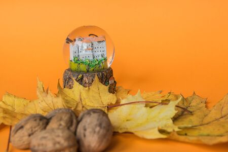 Yellow autumn leaves with nuts and glass sphere on the orange background. Copy space. Flat lay. Top view. Space for text. Greetings composition. の写真素材