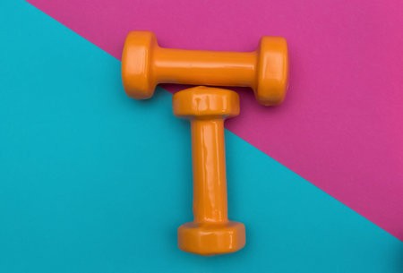 Two orange dumbbells on a pink and blue background. A tool for training, sport and activity in summer time.の写真素材