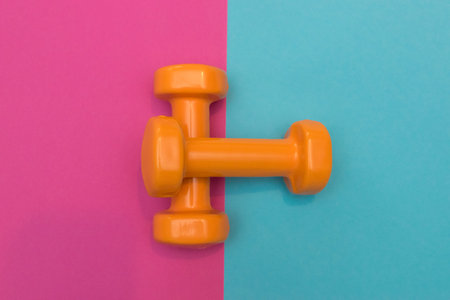 Two orange dumbbells on a pink and blue background. A tool for training, sport and activity in summer time.の写真素材