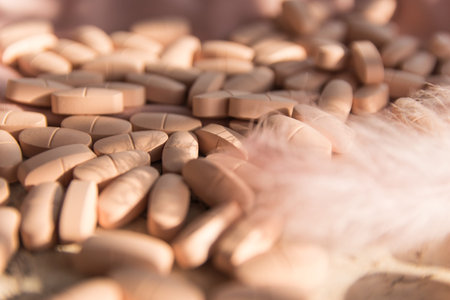 Pills or vitamins on the natural wood background with pink silk fabric and feather in summer day.