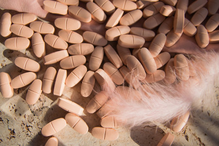 Pink pills or vitamins on the natural wood background with pink silk fabric and feather in summer day.の写真素材