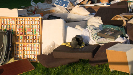 Big garbage with old wood furniture, toys, boxes, plastic bags on a street and green grass in spring...