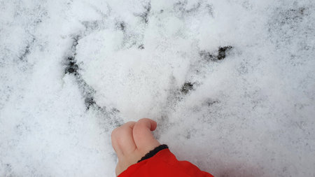 A little girl drawing the heart, a love sign, on a snow covered in the winter time. Romantic background.の写真素材