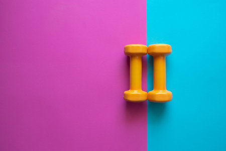 Two orange dumbbells on a pink and blue background with copy space. A tool for training, sport and...