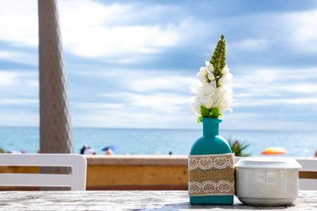 Warehouse on the open air with people. Chairs and tables outside on the summer sun weather. Vase with the flowers on the table for summer cafe with sea view in Spain.の写真素材