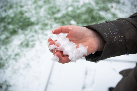 A little child holding the snow in the hand in the garden. Romantic winter background.