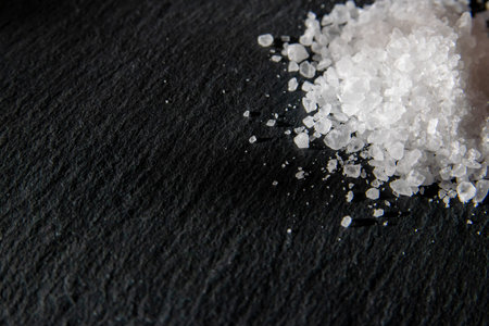Salt crystals for cooking the food. Pile of sea salt on a black natural background.