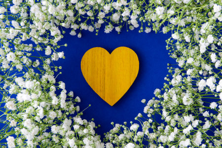 Yellow wood heart on the fabric blau background between little white flowers.の写真素材