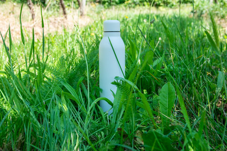 Refreshing water in white thermo stainless bottle on the green grass.の写真素材