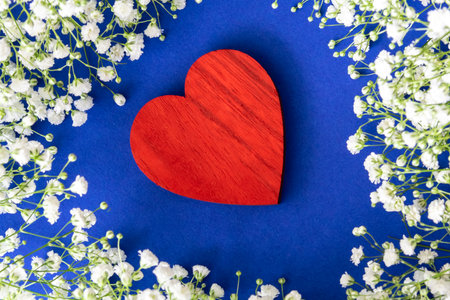 Red wood heart on the fabric blau background between little white flowers.の写真素材