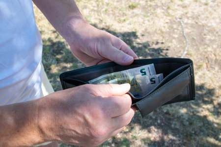 Man holding black leather wallet with bills and coins in the hands. The wallet and money for...