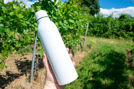 Man holding in the hand white stainless bottle with refreshing water on the nature.の写真素材