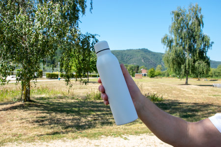 Man holding in the hand white thermo stainless bottle with refreshing water on the nature.の写真素材