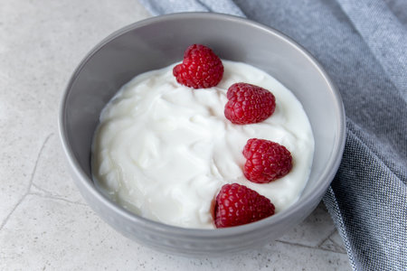 Natural fresh yogurt with raspberry berries in dark plate and napkin for healthy breakfast.の写真素材