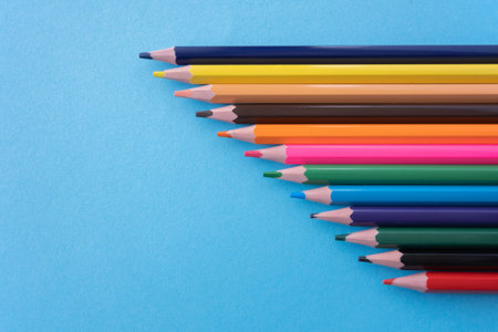 A lot of color pencils on the bright blue paper background. Close up. Design concept. Space for...