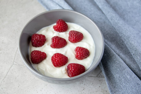 Natural fresh yogurt with red raspberry berries in the gray plate and napkin for healthy breakfast. Stone background.の写真素材