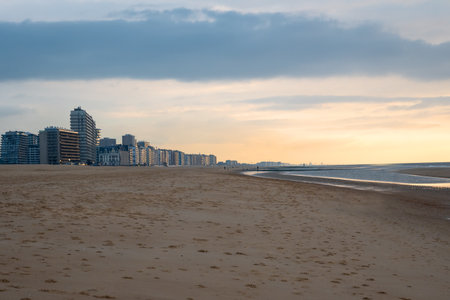 People walking on the sand beach near the sea with a lot of houses and hotel in the evening. Sand, relax and sunset in Ostend, Belgium.の写真素材