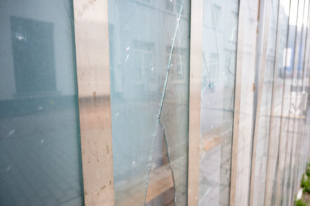 Old broken glass with big and little cracks in close building. Dirty window with protection and view...