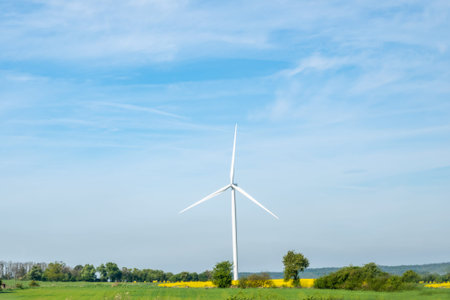 White windmill with green field and blue sky. Wind turbine for alternative green energy in Europe.