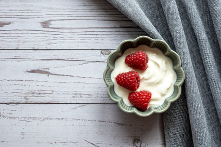 Natural white yogurt with raspberry berries in green plate, wood table and napkin for healthy...