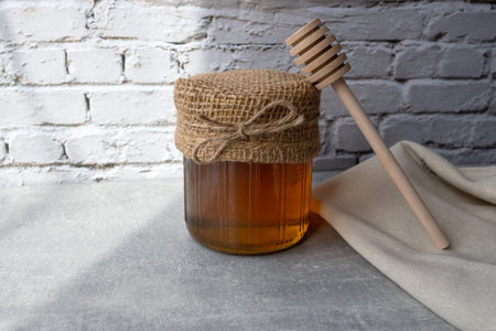 Honey jar with honeycomb and wood spoon stay on the stone table with napkin.