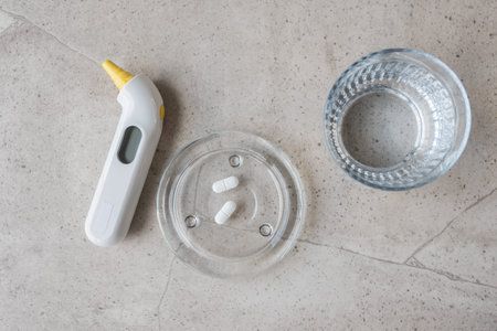 White digital thermometer for temperature, pill and glass with water on the stone table. Healthcare...