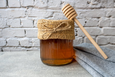 Honey jar with wood spoon stay on the stone table with napkin.の写真素材