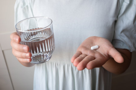 Pill and glass with water in the hand of child. Kid sit at home because of illness.の写真素材