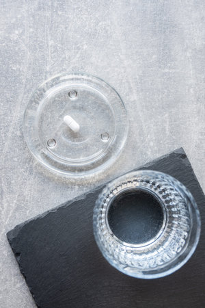 Pill and glass with water on the stone table. Healthcare from pharmacy. Person sit at home because...