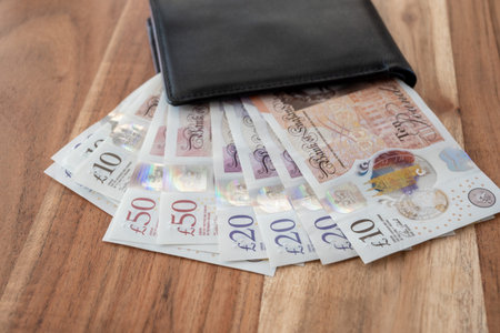 Black leather partmone with British pound money on the wood table. United Kindom bills in leather wallet for commerce concept.の写真素材