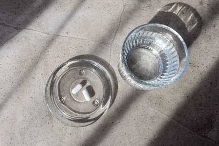 Pill and glass with water on the stone table. Healthcare from pharmacy. Person sit at home because of illness.の写真素材