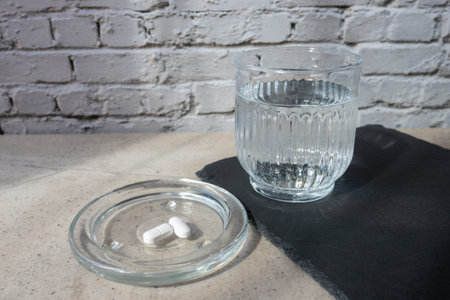 Pill and glass with water on the stone table. Healthcare from pharmacy. Person sit at home because of illness.の写真素材